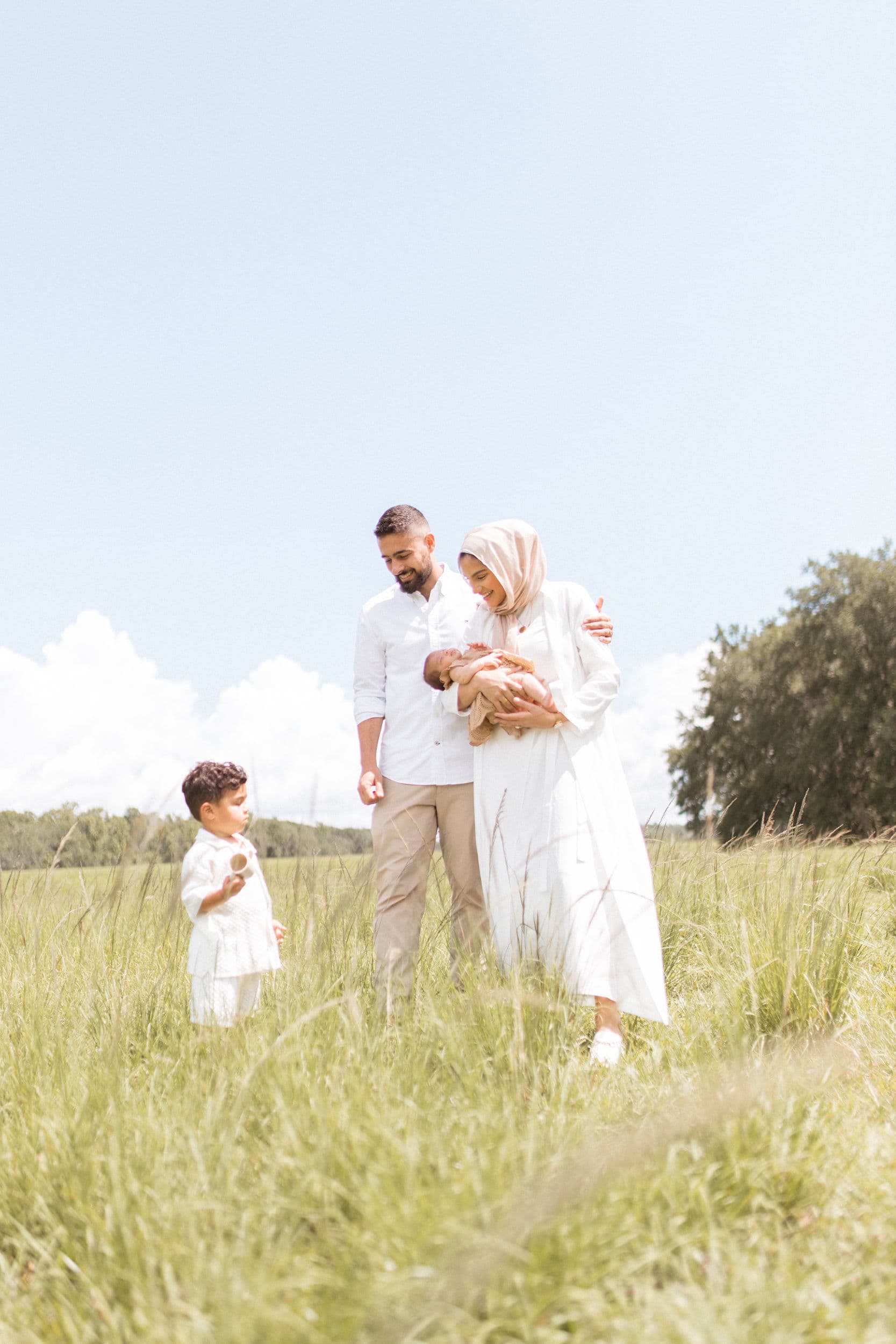 A Muslim family walking together through a green field